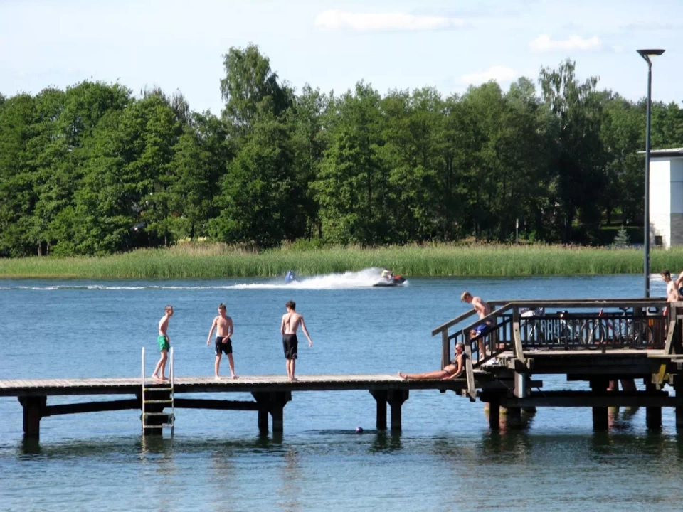 Plaża miejska przy jeziorze Ukiel i pomost, na którym stoją młodzi chłopcy.
