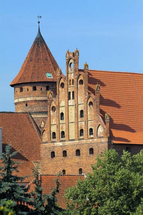 Zamek, który znajduje się w pobliżu Starego Miasta w Olsztynie. Widok na jego zabudowę z czerwonej cegły i wieżę w kształcie rotundy.